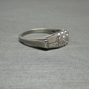 May include: A silver band ring with a row of small, clear diamonds set in a geometric pattern.