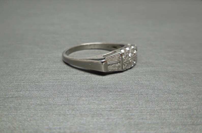 May include: A silver band ring with a row of small, clear diamonds set in a geometric pattern.