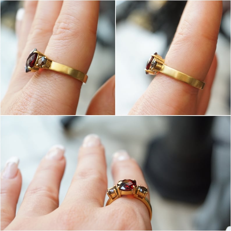 May include: A gold ring with three red gemstones. The ring is on a finger.