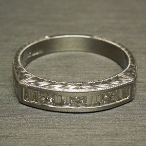 May include: A silver band ring with a decorative engraved design and a row of small diamonds.