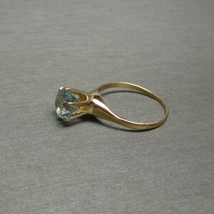 May include: A gold ring with a large, round, light blue gemstone.