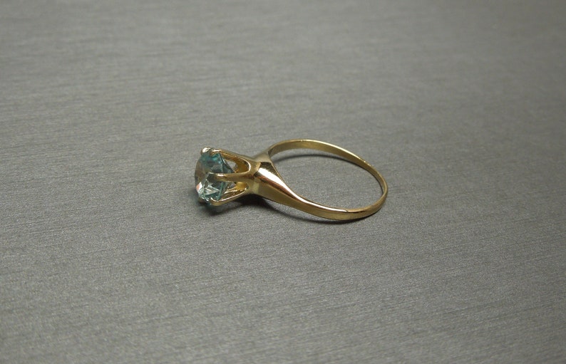 May include: A gold ring with a large, round, light blue gemstone.