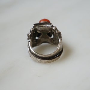 May include: Silver ring with an intricate design and a red gemstone.