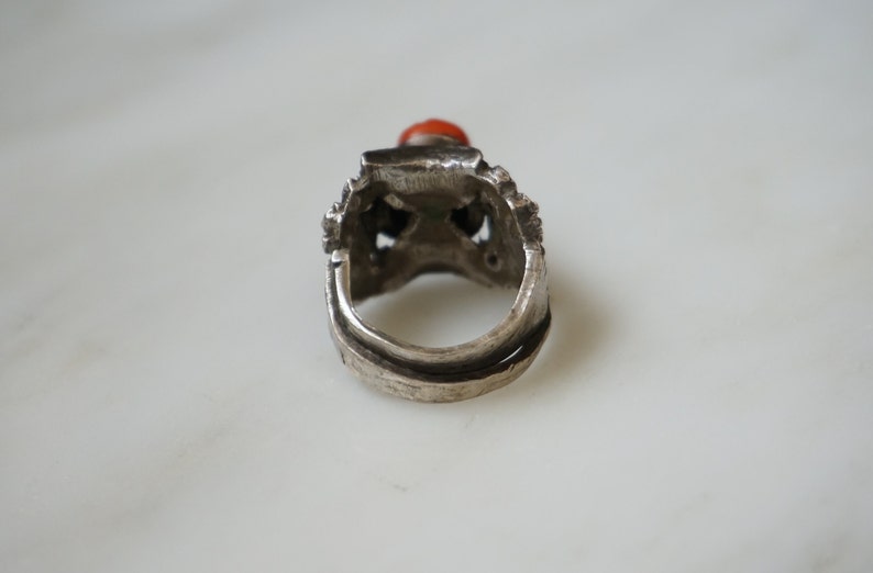 May include: Silver ring with an intricate design and a red gemstone.
