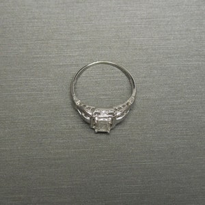 May include: A silver engagement ring with a square-shaped diamond set in a filigree design.