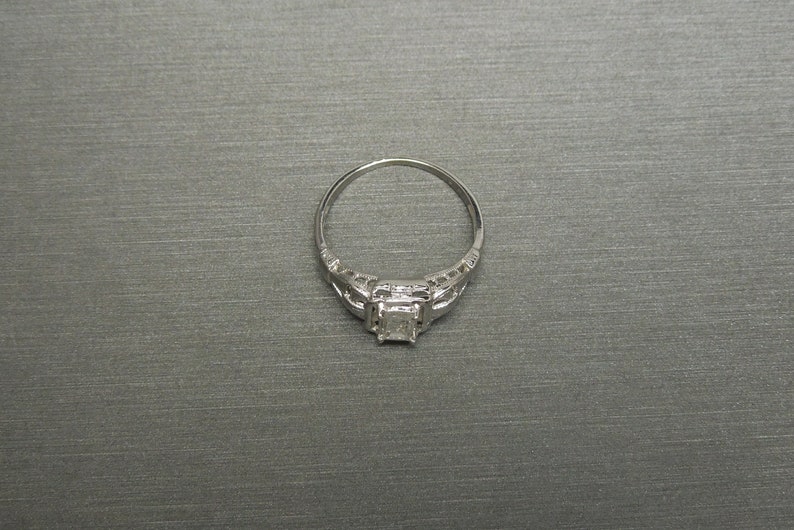 May include: A silver engagement ring with a square-shaped diamond set in a filigree design.