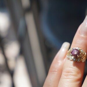 May include: A gold ring with a pink gemstone surrounded by smaller clear gemstones.