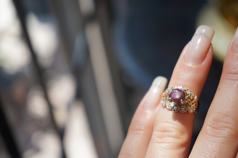 May include: A gold ring with a pink gemstone surrounded by smaller clear gemstones.