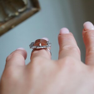 May include: A silver ring with a brown gemstone surrounded by a delicate, intricate design of smaller stones.