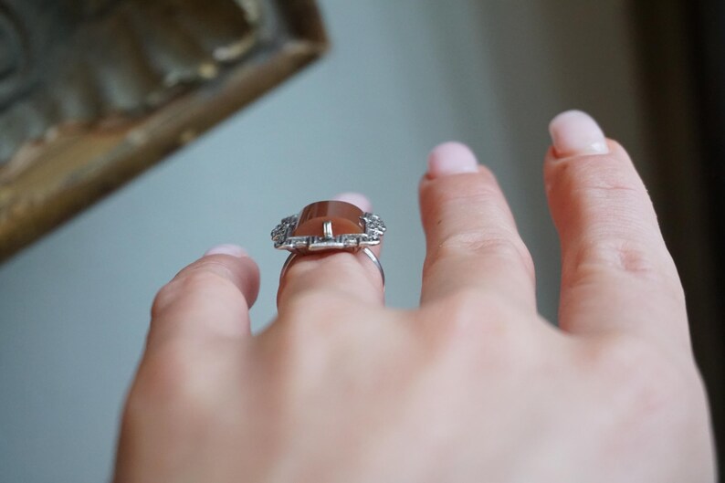 May include: A silver ring with a brown gemstone surrounded by a delicate, intricate design of smaller stones.