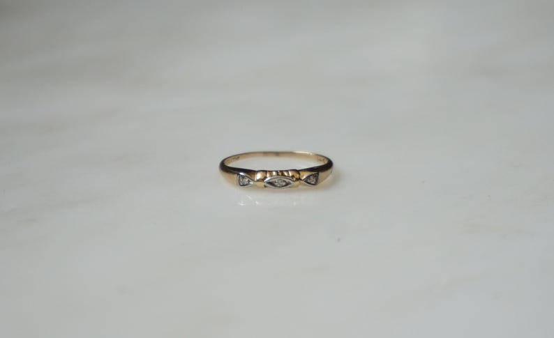 May include: A gold ring featuring three small, clear stones. The ring has a simple band and a decorative design around the stones. The ring is displayed on a white surface.