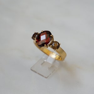 May include: A gold ring with a large, oval-shaped red gemstone surrounded by two smaller, oval-shaped brown gemstones.