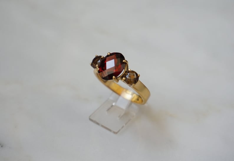 May include: A gold ring with a large, oval-shaped red gemstone surrounded by two smaller, oval-shaped brown gemstones.