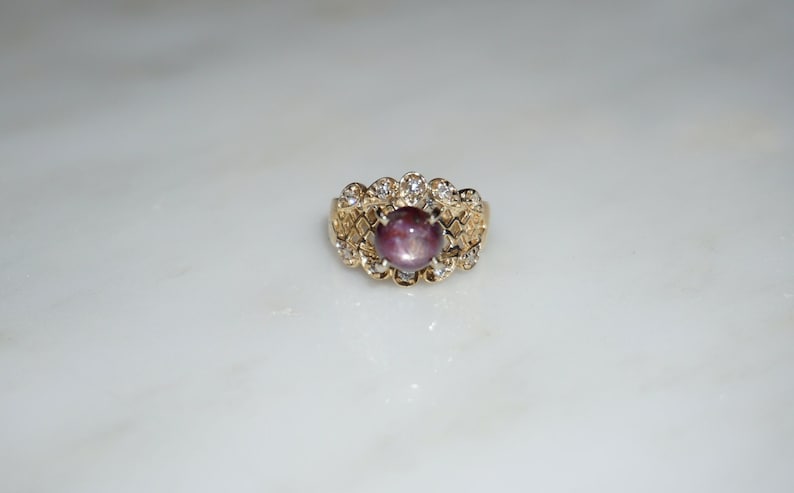 May include: A gold ring with a large, round, purple gemstone surrounded by smaller, clear gemstones.