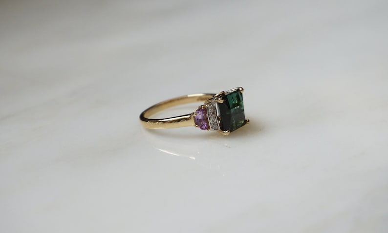 Pu&ograve; includere: Un anello d'oro con una pietra preziosa verde e pietre di accento rosa.