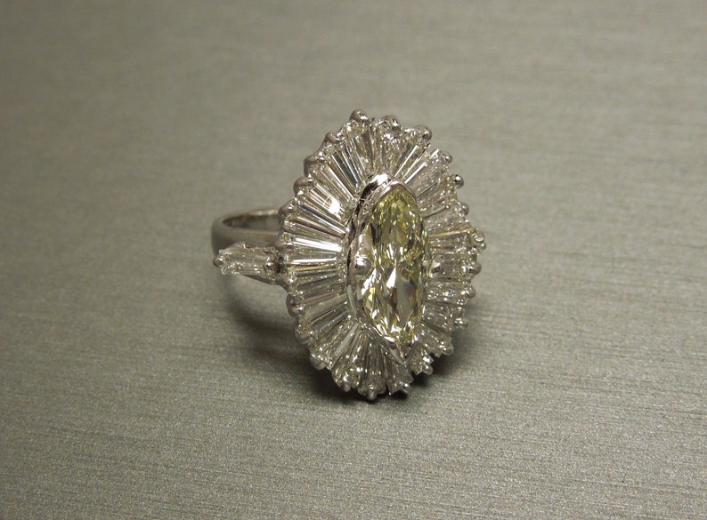 Op de afbeelding: Een zilveren ring met een grote, ovale, gele diamant omringd door kleinere diamanten in een zonnestralenpatroon.