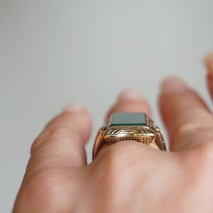 May include: A gold ring with a green gemstone set in a decorative frame.