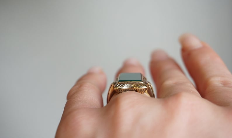 May include: A gold ring with a green gemstone set in a decorative frame.
