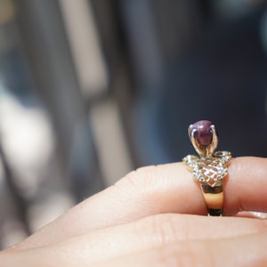 May include: A gold ring with a delicate, intricate design features a single, round, dark purple gemstone.
