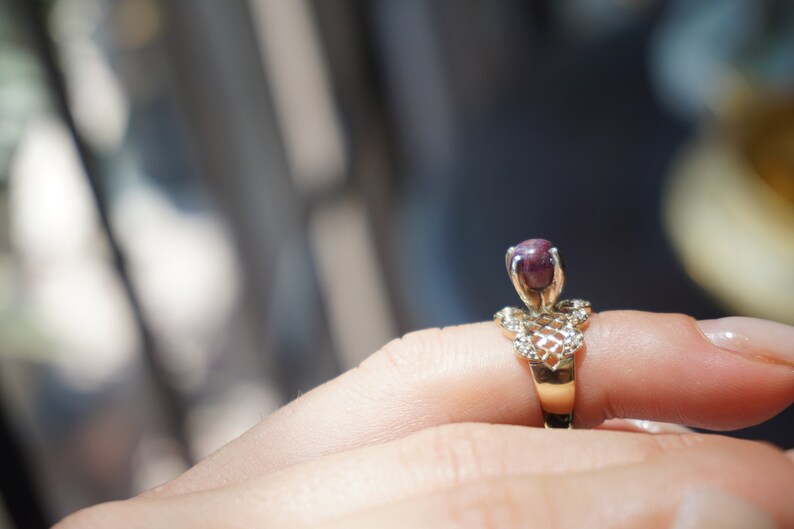 May include: A gold ring with a delicate, intricate design features a single, round, dark purple gemstone.