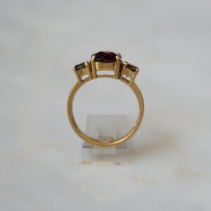 May include: A gold ring with three red gemstones. The center stone is larger than the two stones on either side.