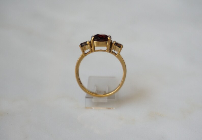 May include: A gold ring with three red gemstones. The center stone is larger than the two stones on either side.