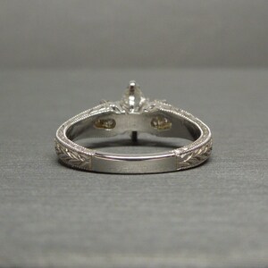 Pode incluir: Um anel de noivado de prata com uma pedra central de diamante e dois diamantes menores na banda. A banda &eacute; gravada com um design floral.