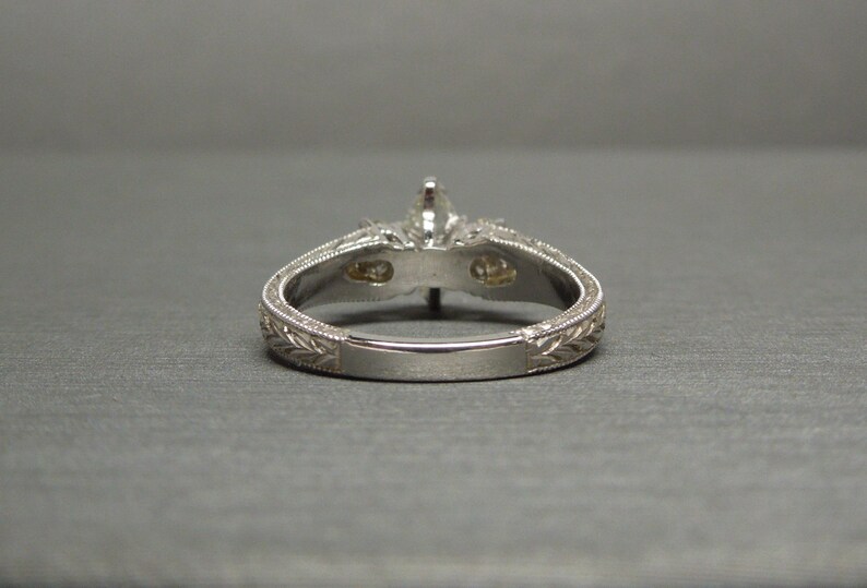 Pode incluir: Um anel de noivado de prata com uma pedra central de diamante e dois diamantes menores na banda. A banda &eacute; gravada com um design floral.