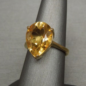 May include: A gold ring featuring a large pear-shaped topaz gemstone. The gemstone is a bright yellow colour.