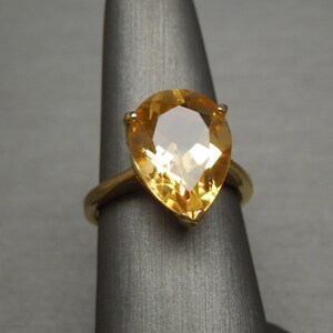 May include: A gold ring featuring a pear-shaped topaz gemstone. The gemstone is a light yellow colour and has a faceted cut.