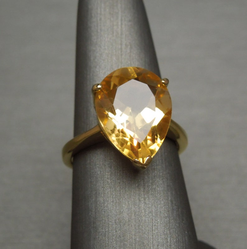 May include: A gold ring featuring a pear-shaped topaz gemstone. The gemstone is a light yellow colour and has a faceted cut.