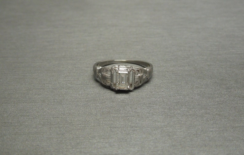 May include: A silver ring with an emerald-cut diamond set in a delicate filigree design.