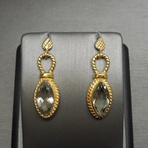 May include: A pair of gold earrings with a green gemstone in the centre of each earring. The earrings are shaped like a teardrop and have a delicate design.