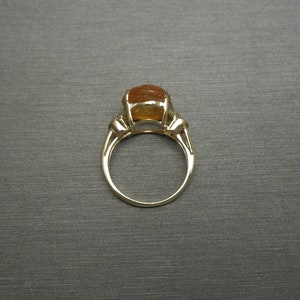 May include: A gold ring with a large, oval-shaped, orange gemstone. The ring has a simple band and three small accent stones on each side of the gemstone.