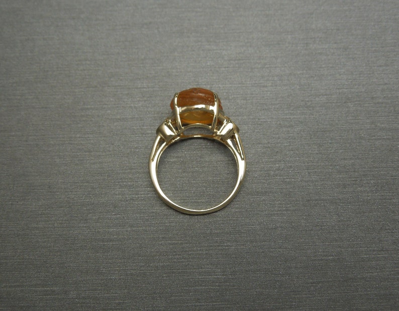 May include: A gold ring with a large, oval-shaped, orange gemstone. The ring has a simple band and three small accent stones on each side of the gemstone.