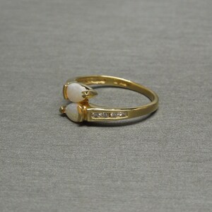 K&ouml;nnte beinhalten: Ein goldener Ring mit zwei wei&szlig;en Opal-Steinen und einer Reihe kleiner, klarer Diamanten.