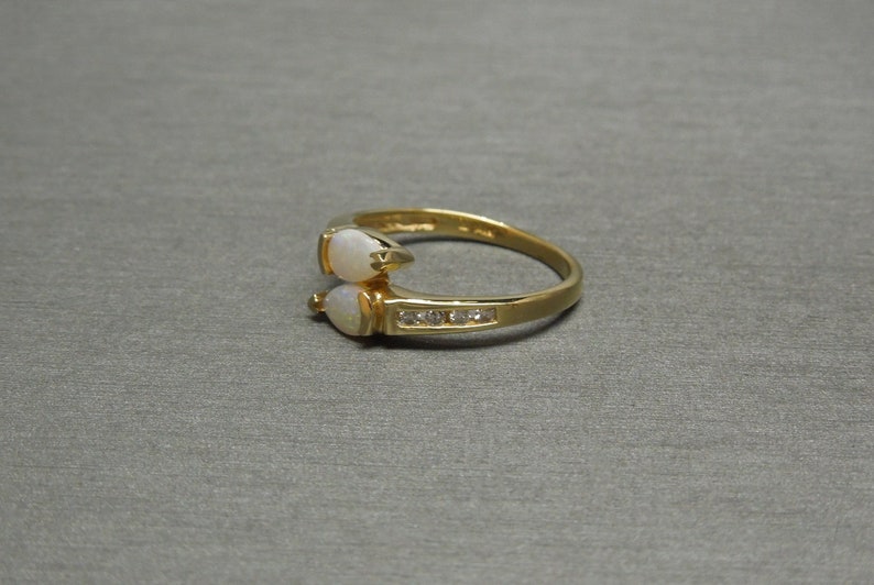 K&ouml;nnte beinhalten: Ein goldener Ring mit zwei wei&szlig;en Opal-Steinen und einer Reihe kleiner, klarer Diamanten.