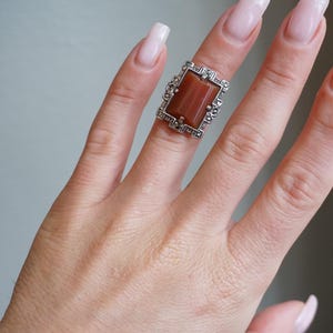May include: A silver ring with a rectangular brown stone set in a detailed filigree design.