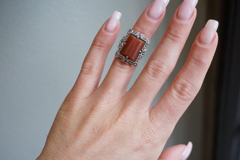 May include: A silver ring with a rectangular brown stone set in a detailed filigree design.