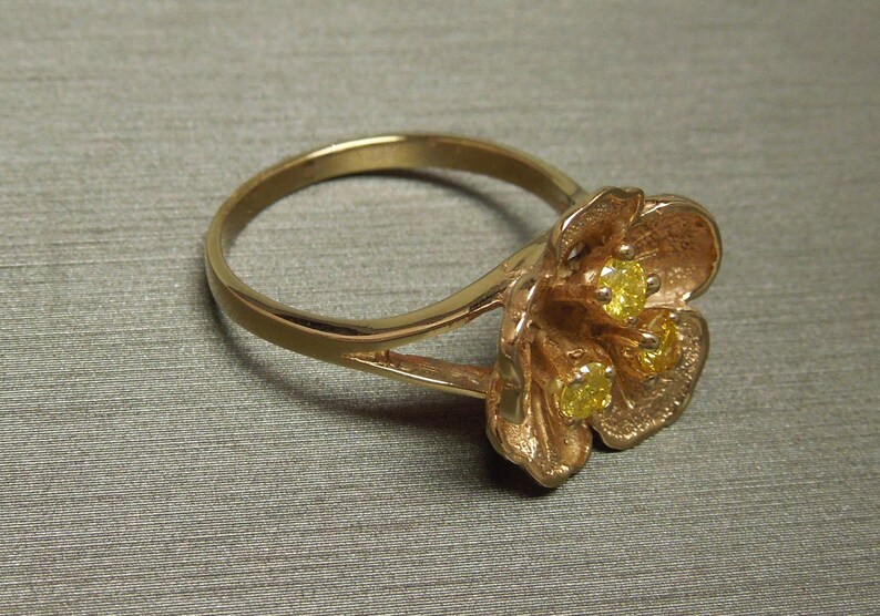 May include: A gold ring with a flower design featuring three yellow gemstones.