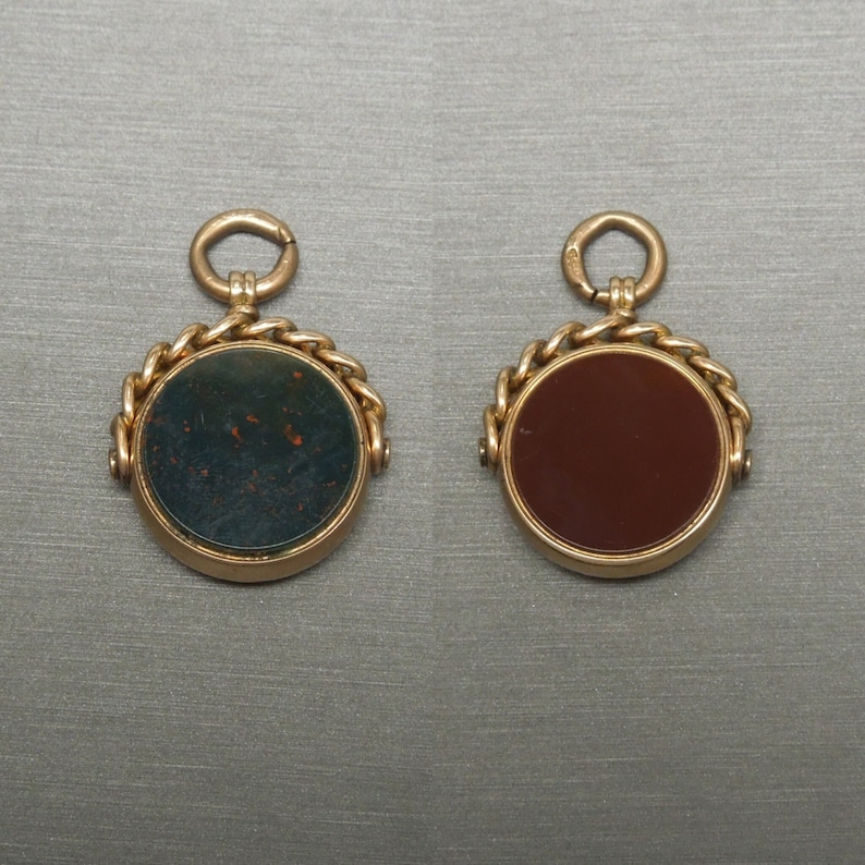 May include: Two gold fobs with round, decorative, swiveling frames. One fob has a dark green stone and the other has a reddish-brown stone.