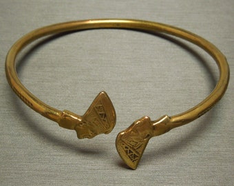 May include: A gold-colored metal bracelet with two decorative ends. The ends are shaped like a stylized axe head with geometric patterns.