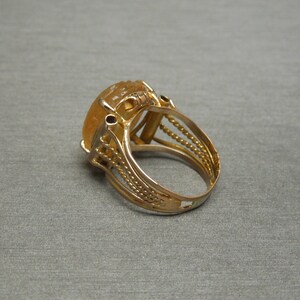 Op de afbeelding: Een gouden ring met een grote, ovale, gele edelsteen gezet in een filigraan ontwerp.