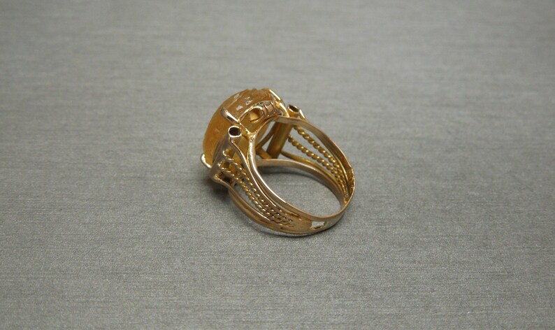 Op de afbeelding: Een gouden ring met een grote, ovale, gele edelsteen gezet in een filigraan ontwerp.