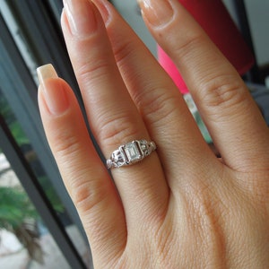 May include: A silver ring with an emerald-cut diamond set in a delicate filigree design.