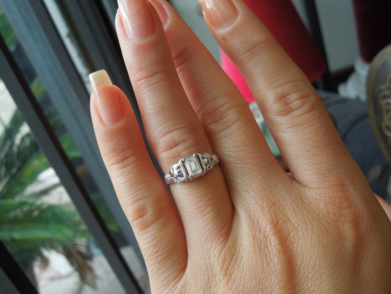 May include: A silver ring with an emerald-cut diamond set in a delicate filigree design.