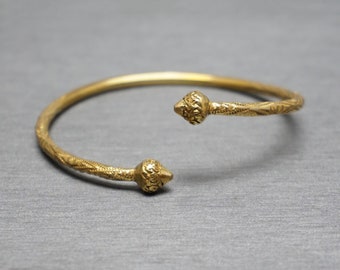 May include: A gold bangle bracelet with a decorative design and pointed ends.