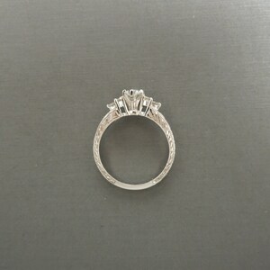Pode incluir: Um anel de prata com tr&ecirc;s diamantes engastados em garras. A banda &eacute; decorada com um delicado design gravado.