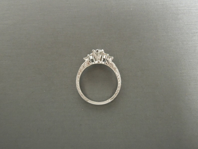 Pode incluir: Um anel de prata com tr&ecirc;s diamantes engastados em garras. A banda &eacute; decorada com um delicado design gravado.