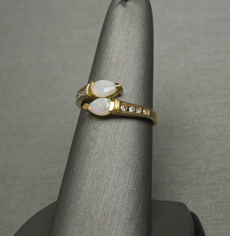 K&ouml;nnte beinhalten: Ein goldener Ring mit zwei birnenf&ouml;rmigen Opalen und einer Reihe kleiner Diamanten.